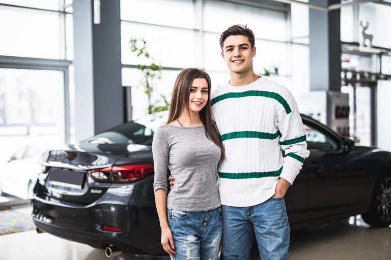 Smiling couple standing in front of a car at new car